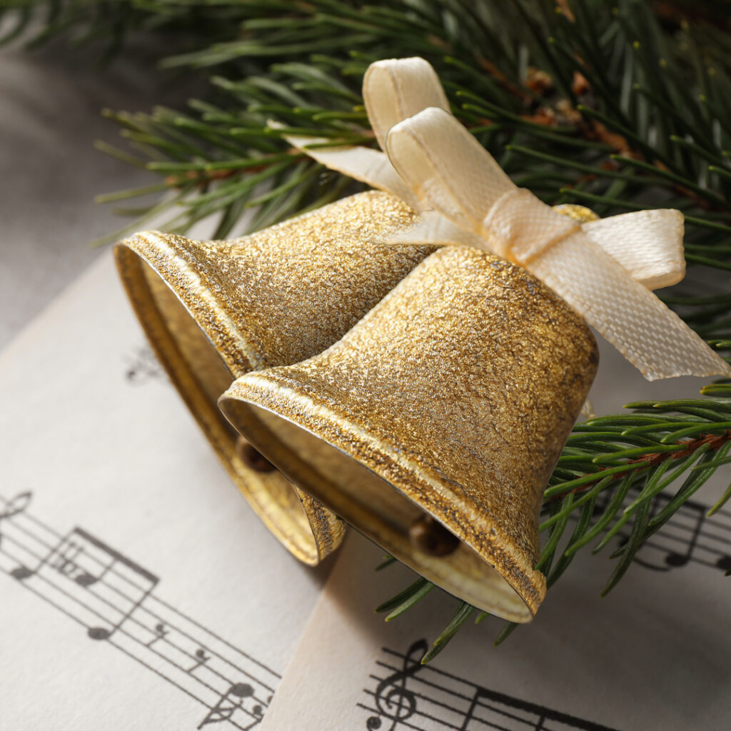 2 decorative golden bells of christmas laid over a musical sheet