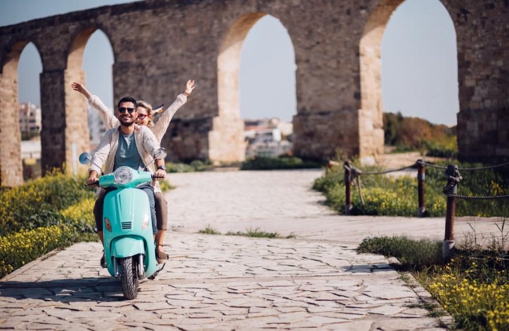 Two people riding together on a light blue vespa.